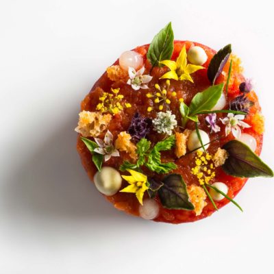 Tomato Lobster Disc Tomato lobster disc garnished with croutons, chervil, chive tips, lemon gel, bonito mayonnaise, tomato flowers, fennel flowers, and basil on a white surface. Prepared by Daniel Humm at Eleven Madison Park.